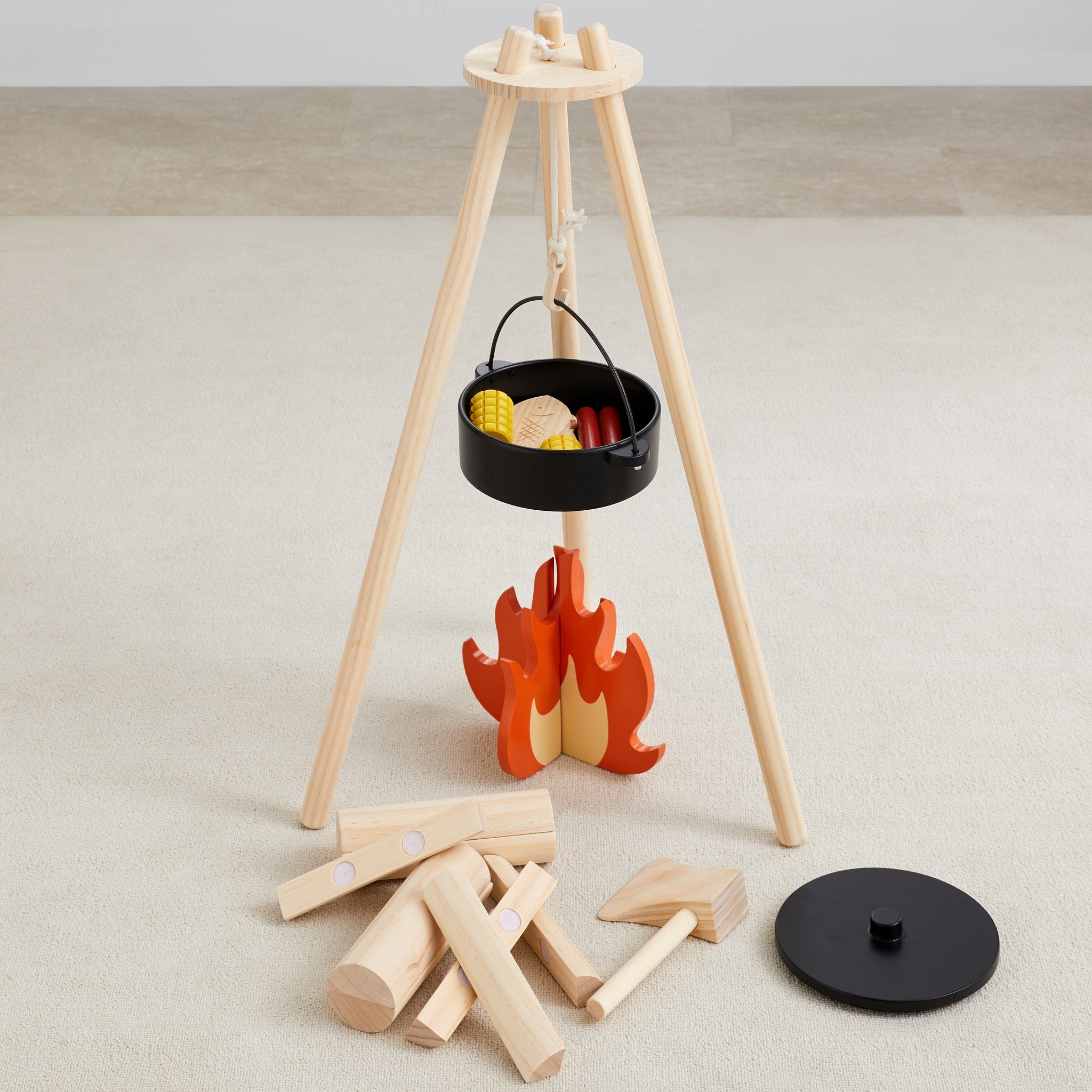 Home on the Range wooden tripod with hanging black pot over an orange flame, logs, ax and lid laid out below