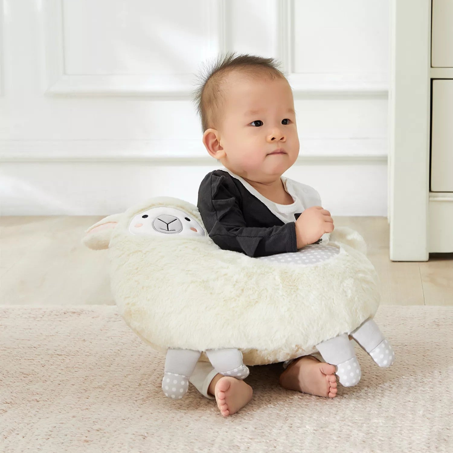 Baby sitting on white llama stuffed animal plush toy in nursery