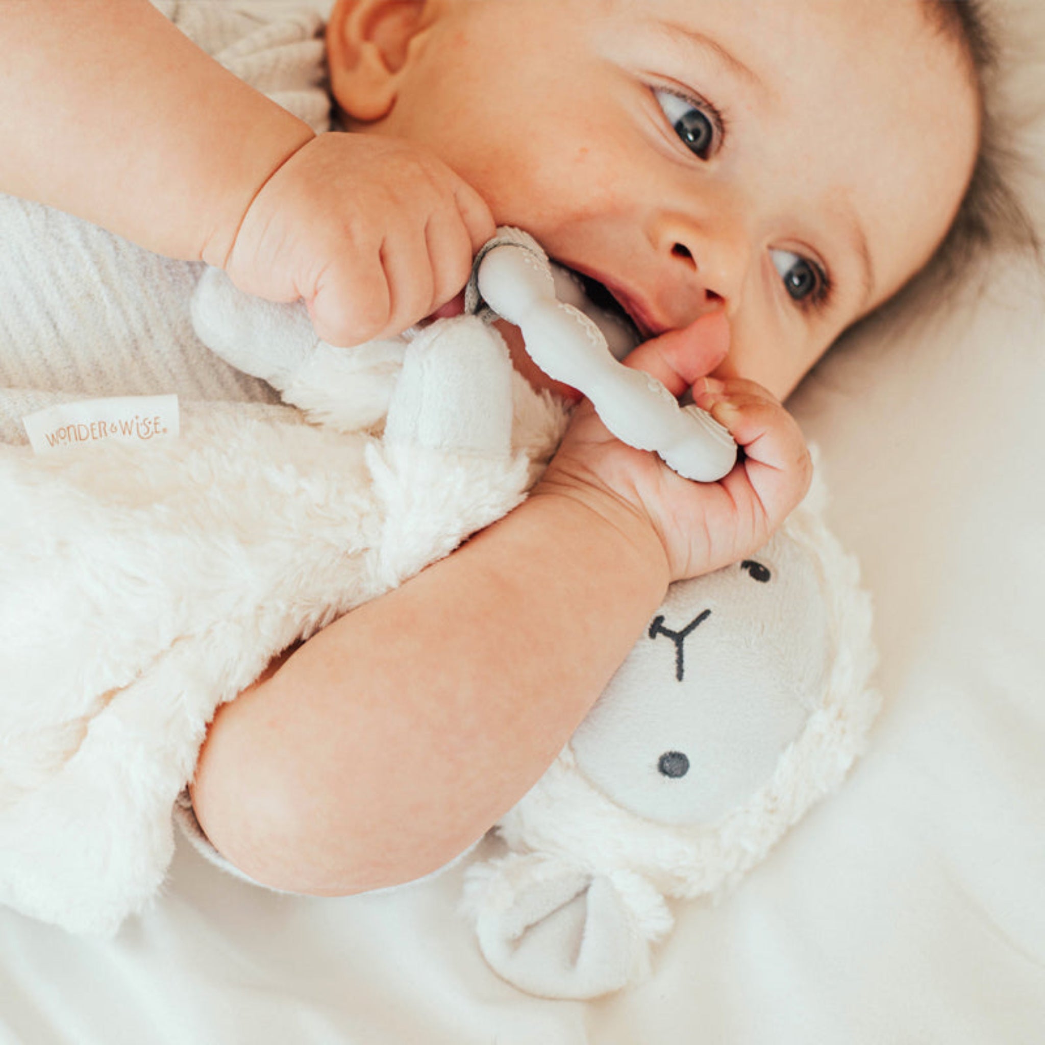 Baby chewing on cream colored soft lovey toy with simple face design