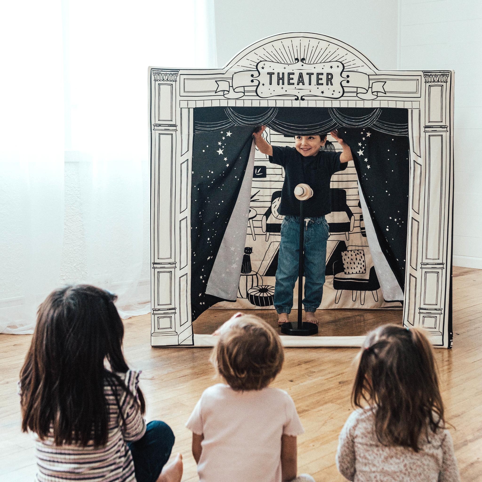 Child opening the starry curtains of the Performance Stage while three children watch from the floor