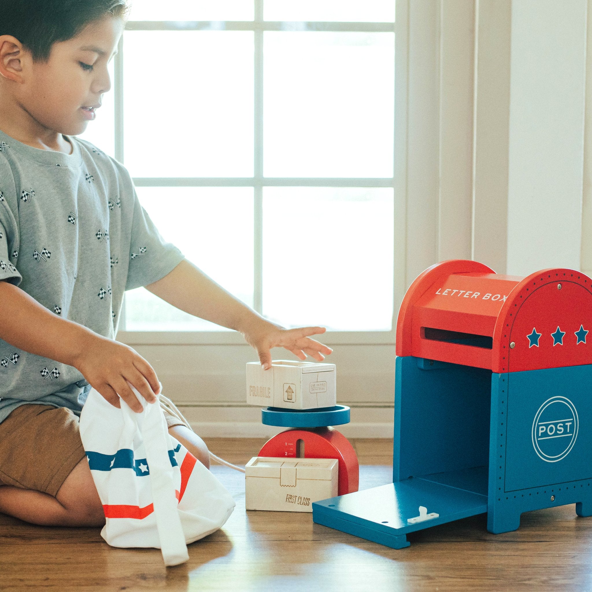 Child kneeling by a window with the Extra Special Delivery Mail Set mail bag, packages and letter box