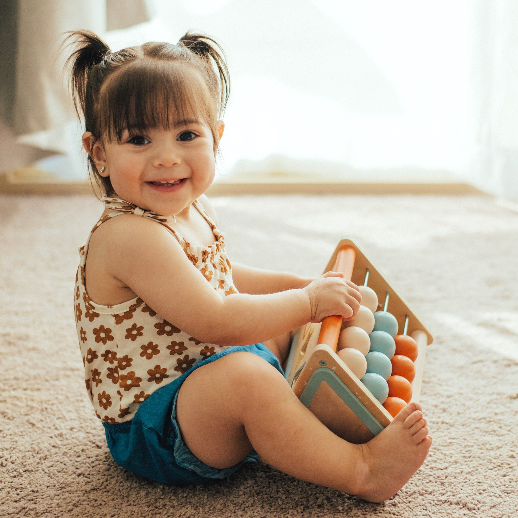 Smiling baby sitting on carpet holding the Playful Triangle with its abacus beads showing