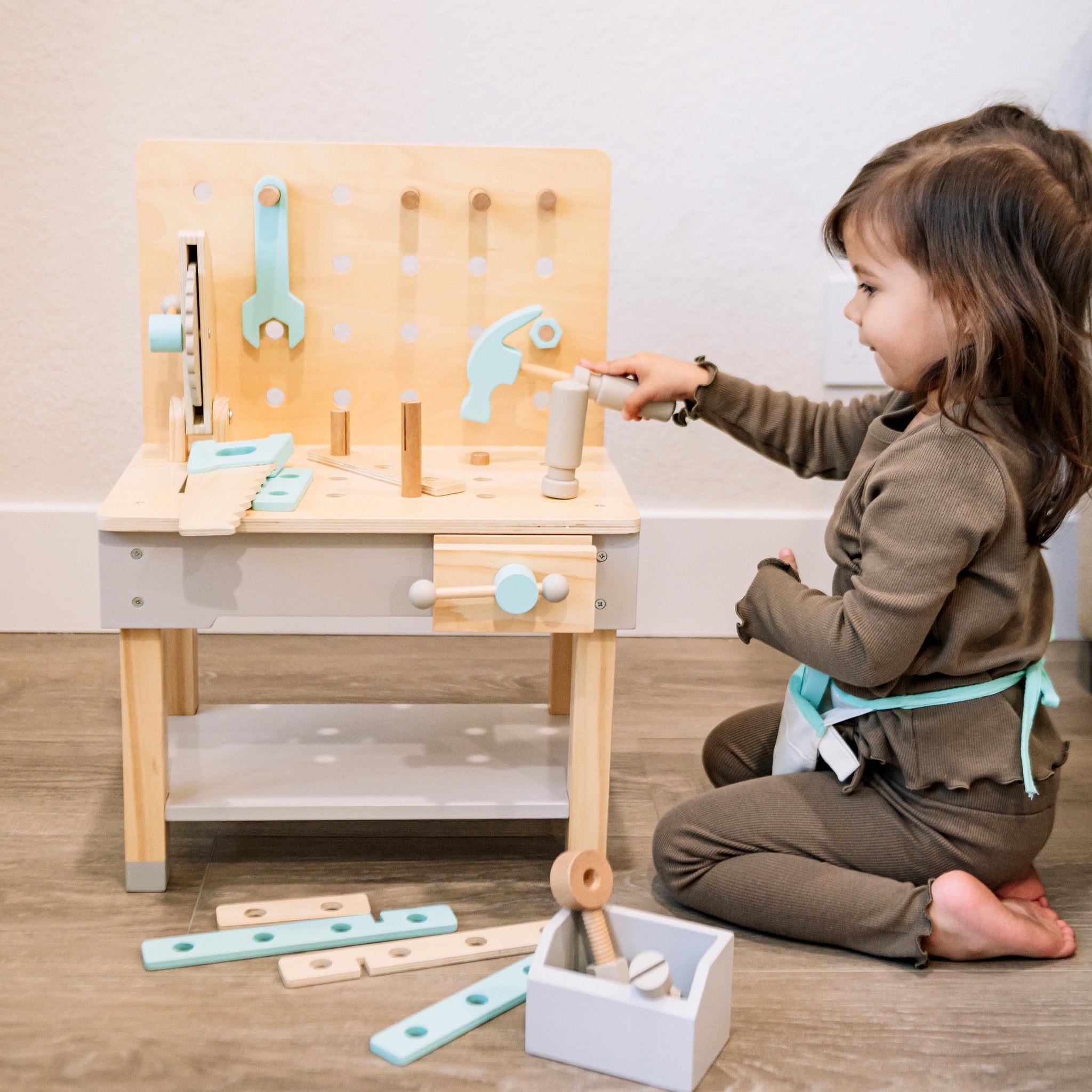 Child kneeling at the Little Builder Workbench using the toy hammer, boards and bin on the floor