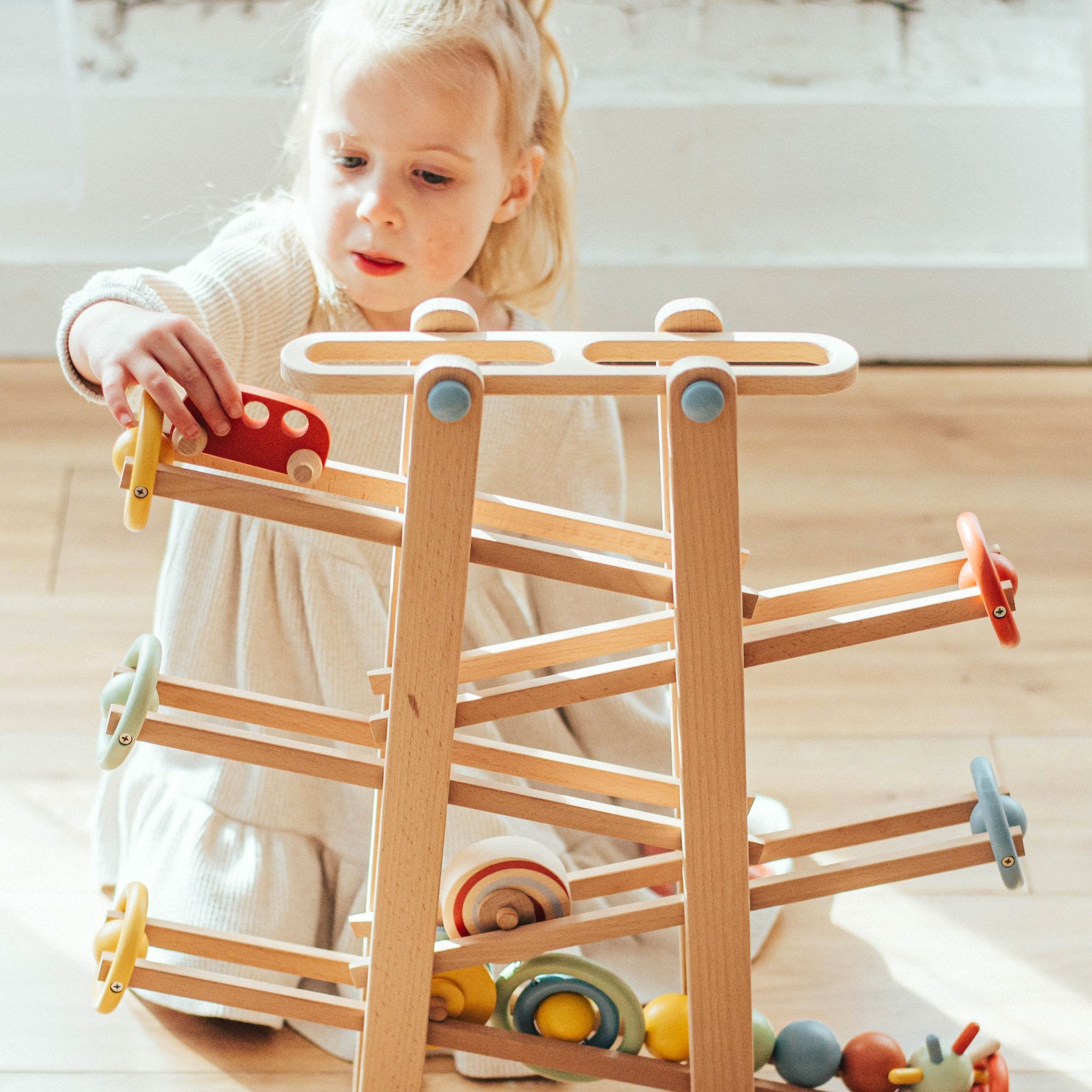 Child placing a red wooden car at the top ramp of the Tumble Track, pastel wheel bumpers at each ramp end