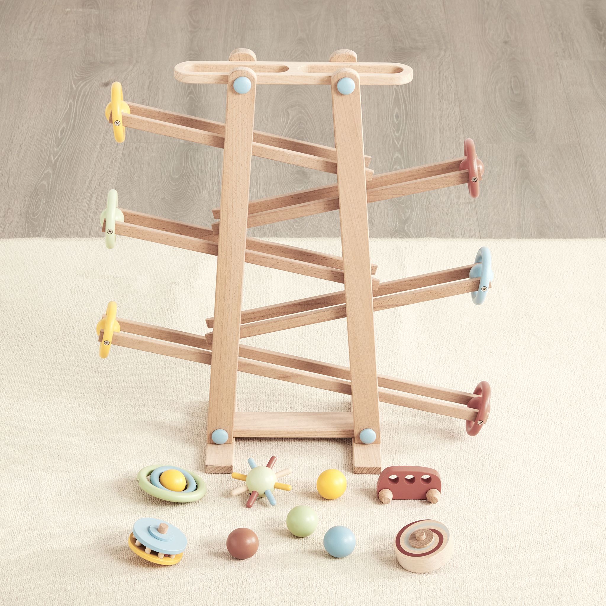 Tumble Track wooden zigzag ramp on carpet with its rolling pieces lined up in front: balls, car, spinner and discs