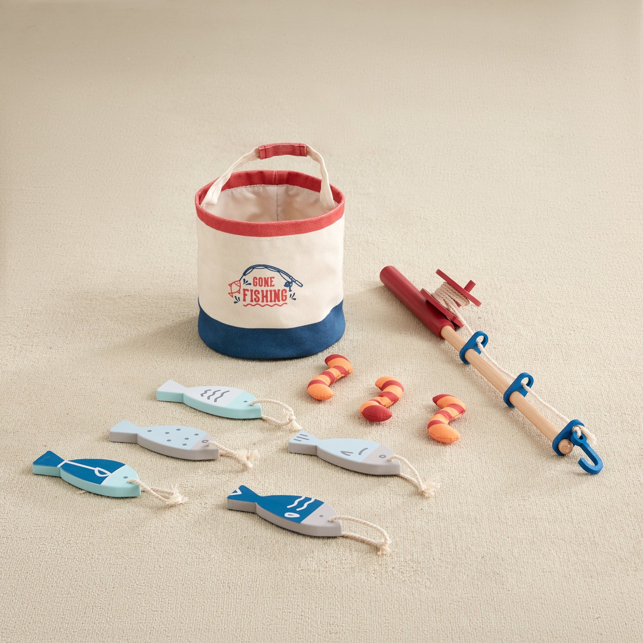 Gone Fishing Set with canvas bucket, wooden fishing rod, five wooden fish, and three striped fabric worms laid out on cream carpet